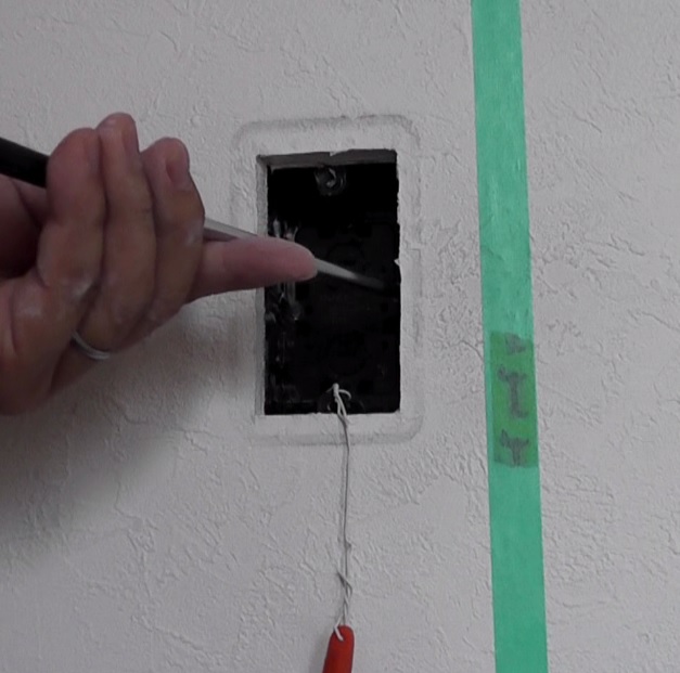 ケーブルが通されていないコンセントボックスを間柱にネジ固定する際にはボックスが誤って壁内に落ちないようストッパーをつけて作業する