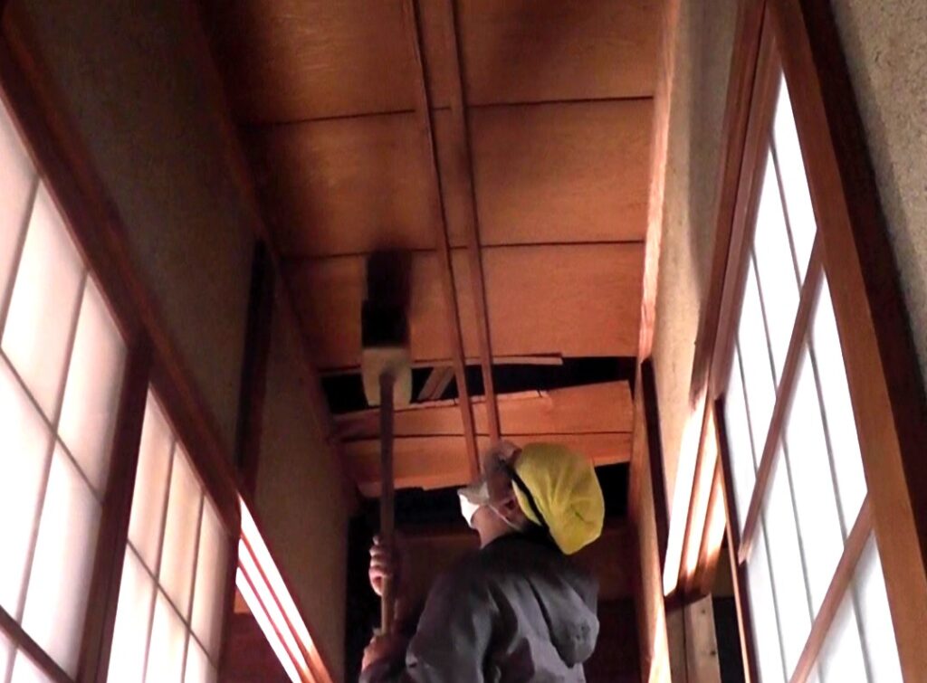 実家の古民家の中央廊下の天井板を大型の木槌である掛け矢を使用して剥がす